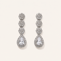 A pair of silver-tone drop earrings adorned with clear pavé gemstones, featuring a stacked floral design and a teardrop-shaped center stone, displayed on a light cream background.